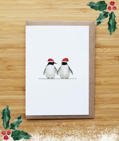 two penguins wearing red hats sitting on top of a wooden table next to holly leaves