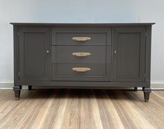 a grey dresser with gold handles on it's doors and drawers, against a white wall