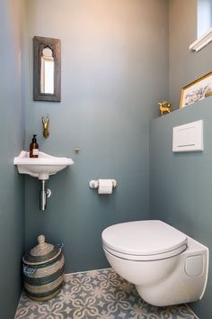 a white toilet sitting next to a sink in a bathroom under a painting on the wall