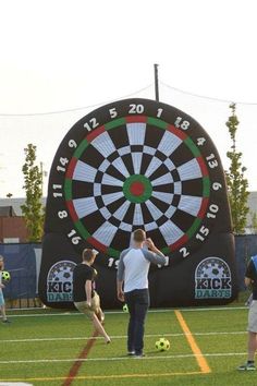 a group of people standing on top of a lush green field next to a dart board