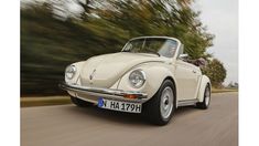 an old white car driving down the road with trees in the backgrouund