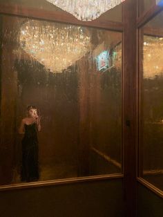 a woman taking a selfie in front of a mirror with chandelier hanging from the ceiling