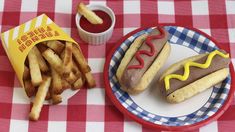 two hot dogs and french fries on a plate next to a cup of ketchup