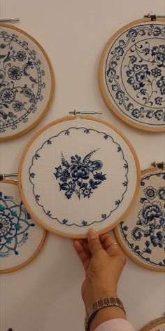 a person is holding up some blue and white embroiderys on the wall above them