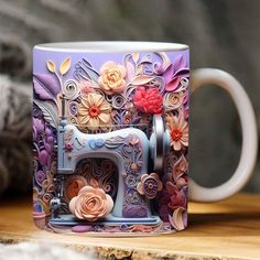 a coffee mug with a sewing machine and flowers painted on the side sitting on a table