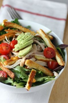 a white bowl filled with salad and french fries on top of a wooden table next to a fork