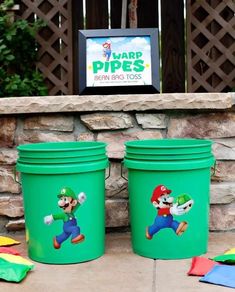 two green buckets with mario and luigi on them sitting in front of a sign