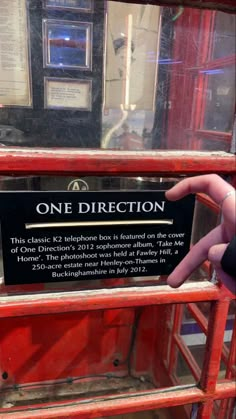 there is a sign that says one direction in front of a red phone booth with information on it