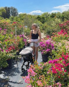 a woman is walking with her baby in a stroller through the flowerbeds