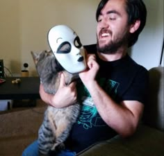 a man holding a cat with a mask on it's face in front of his face