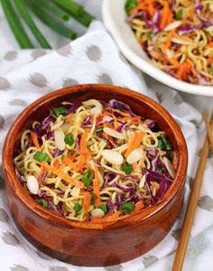 a wooden bowl filled with noodles and vegetables next to chopsticks