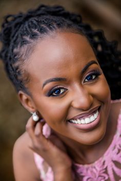 a smiling woman with braids on her hair, wearing a pink top and earrings