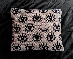 a black and white knitted pillow with hand prints on the front, sitting on a bed