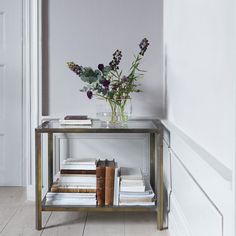 a glass table with books and flowers on it in front of a white painted wall