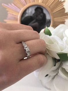 a woman's hand with a wedding ring on it and flowers in the background