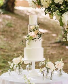 a wedding cake with flowers and greenery on the top is surrounded by small vases