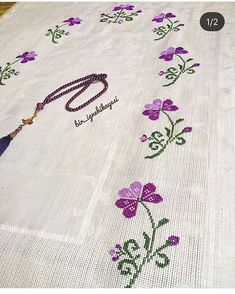 an embroidered tablecloth with purple flowers on it and a tassel hanging from the end