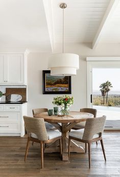 the dining room table is surrounded by chairs and a vase with flowers on it in front of an open window