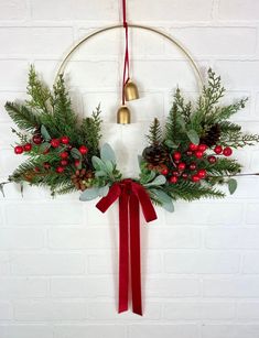 a christmas wreath hanging on a brick wall with bells and greenery around the wreath