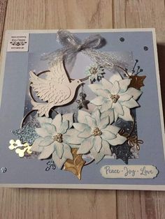 a card with some white flowers and a dove on it's side, sitting on a wooden surface