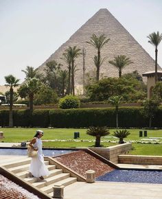 a woman in white dress standing on steps near pyramid