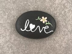 a black rock with the word love painted on it and flowers in white writing that says love