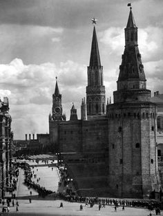 an old black and white photo of people walking in front of some very tall buildings