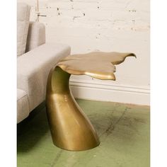 a gold leaf shaped table sitting on top of a green floor next to a couch