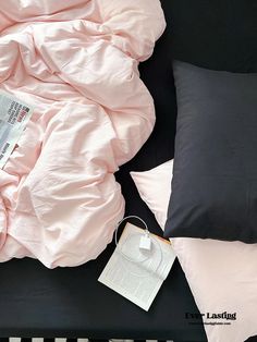 an unmade bed with pink sheets, pillows and a magazine on the floor next to it