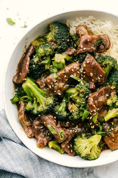 a bowl filled with beef and broccoli on top of rice covered in sesame seeds