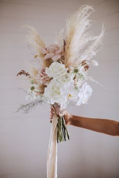 a person is holding a bouquet with flowers and feathers on the stems in their hands