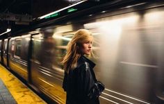 a woman standing in front of a train at a subway station, with her head turned to the side