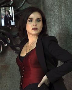 a woman in a red top and black blazer posing for the camera with her hands on her hips