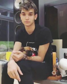 a young man sitting on top of a table holding a small brown and white dog