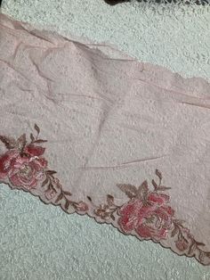 a pink lace with flowers on it laying on a bed sheet next to a black cat