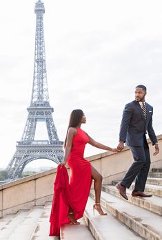 a man and woman in front of the eiffel tower holding hands while walking up some steps