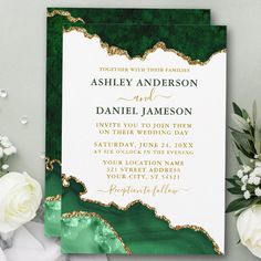 a green and gold wedding card with white flowers on the side, next to it