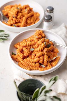 two white bowls filled with macaroni and cheese on top of a table next to silverware