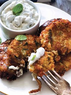 two crab cakes on a plate next to a bowl of whipped cream and a fork