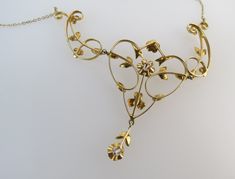 "Petite floral elements, swirling gold vines, tiny seed pearls and diamonds make up this beautiful antique 14k gold lavalier necklace. The artistic styling of this early 1900s piece is reminiscent of Victorian and Edwardian design. The necklace is composed with four main components, the gold chain, focal pendant and two fancy metalwork links flanking it. Most of the gold leaves and flower shapes are set with 0.5mm - 1mm seed pearls. Two are set with diamonds. The central pendant has a 2.1mm .01 Vintage Yellow Gold Necklace With Diamond Accents, Victorian Wedding Necklaces With Diamond Accents, Antique Necklace With Diamond Accents, Antique Necklaces With Diamond Accents, Antique Yellow Gold Necklace With Diamond Accents, Gold Art Nouveau Necklace With Intricate Design, Art Nouveau Gold Necklace With Intricate Design, Vintage Gold Necklace With Rose Cut Diamonds, Antique Gold Necklace With Diamond Accents