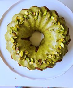 a green cake with pistachios on top sitting on a white platter