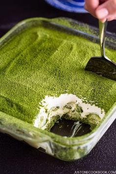 someone is scooping out some green food from a dish in a glass pan with a spoon