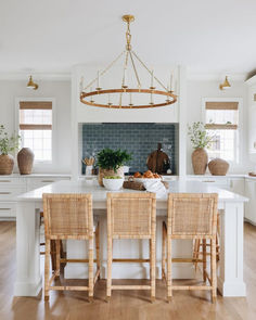 a kitchen with white cabinets and wooden chairs in front of a large center island topped with potted plants