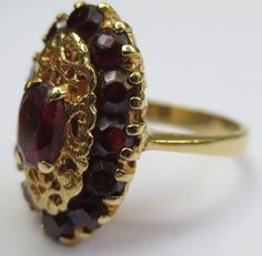 This ring looks so regal! The deep red garnets against the rich colored 18k gold compliment each other beautifully. Dating from the early 1900's-40's and hallmarked in the interior 750 and 176AAL. Has been tested to ensure the golds purity. Rings size is 6 1/2 and is ready to be worn and admired! The halo setting measures 11/16 by 7/16 of an inch. Stones are all held securely in place. Center garnet measures 6.12mm by 4.25mm. Some stones have light surface wear as to be expected with a ring of s Elegant Garnet Ruby Ring Stamped 14k, Vintage Multi-stone Ruby Ring, Antique Hallmarked Ruby Ring, Victorian Oval Ruby Ring In Yellow Gold, Victorian Gold Ruby Ring For Formal Occasions, Victorian Ruby Ring For Formal Occasion, Formal Multi-stone Garnet Rings, Antique Yellow Gold Multi-stone Ruby Ring, Vintage Ruby Multi-stone Rings