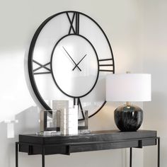 a black and white clock sitting on top of a table next to a lamp in a room