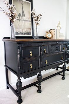 a black dresser with two vases on top of it next to a clock and flowers