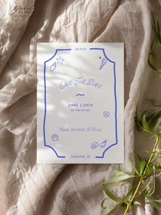 save the date card with blue ink on white paper next to green leaves and branches