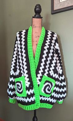 a green and black crocheted sweater on a mannequin head stand in front of a wall