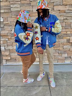 two people standing next to each other in front of a brick wall wearing jackets and hats