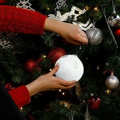 two hands are decorating a christmas tree with ornaments and balls on it, while another hand is holding a white ball